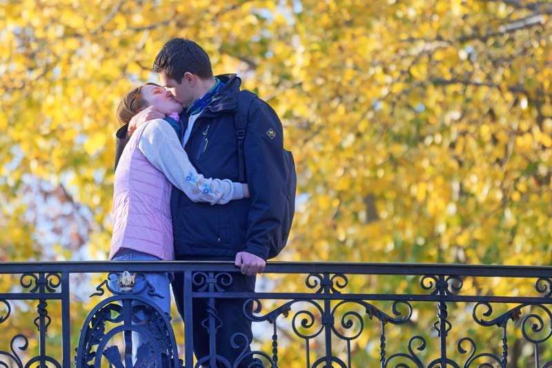 29 - Young couple kissing by a decorative iron railing against a vibrant autumn backdrop
